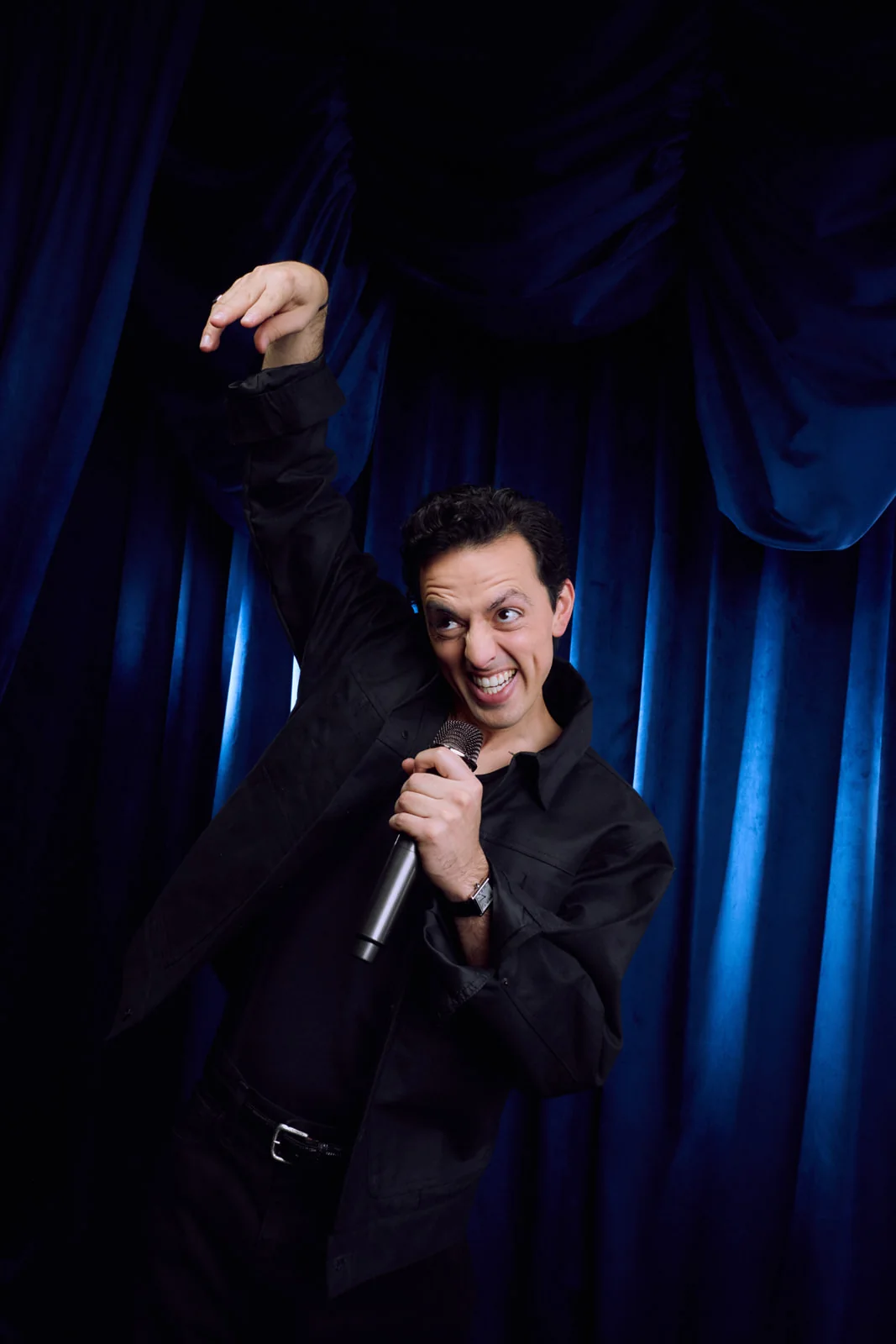 José Ramones haciendo stand up con micrófono frente a cortinas azules