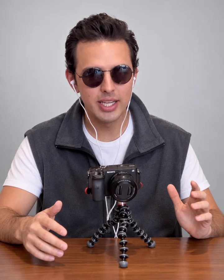 José Ramones en el personaje del podcast, con lentes oscuros, micrófono y cámara sobre la mesa